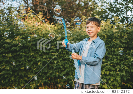 A boy is playing with soap bubbles in a summer park, Among the greenery. A boy is playing with soap bubbles in a summer park, Among the greenery. 92842372