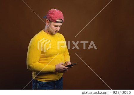 Charming plump young man thoughtfully writes a message on the phone, standing portrait Charming plump young man thoughtfully writes a message on the phone, standing portrait 92843090