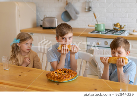 Cheerful children are sitting at table in kitchen, playing with loaf bread Cheerful children are sitting at table in kitchen, playing with loaf bread 92844329
