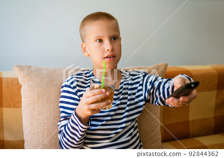 Young man watches tv, using remote control to change channels. Guy got bored Young man watches tv, using remote control to change channels. Guy got bored 92844362
