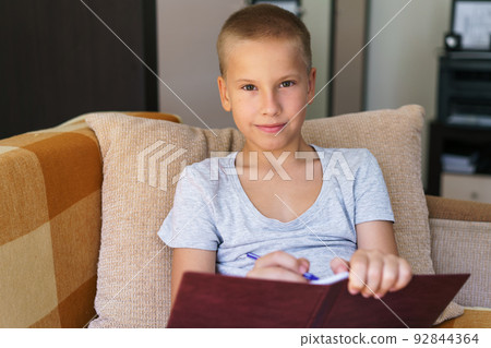 Portrait of schoolboy sitting on sofa doing homework, happy child, boy holding Portrait of schoolboy sitting on sofa doing homework, happy child, boy holding 92844364