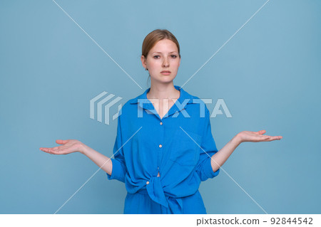 Young woman in shirt on blue background, pointing to side with both hands 92844542