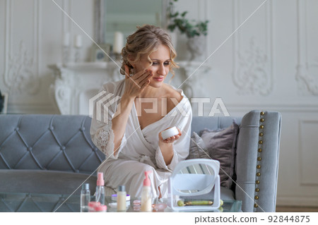 Pretty european woman applies facial cream on her face holds jar cosmetic Pretty european woman applies facial cream on her face holds jar cosmetic 92844875