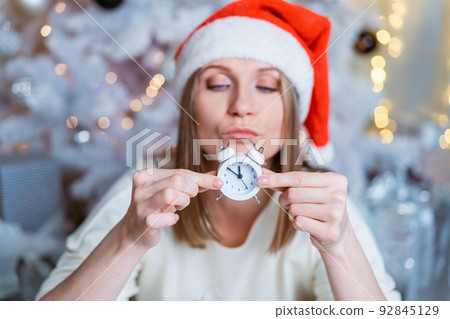 Portrait of a caucasian woman with an alarm clock in her hand and a santa hat Portrait of a caucasian woman with an alarm clock in her hand and a santa hat 92845129