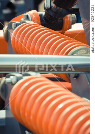 Big and hard orange steel spring as part and detail of industrial or agricultural machine 92845222