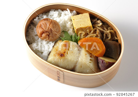 一個銀鱈魚西京燒便當盒的鳥瞰圖,在米飯和玉子燒上放著一個大醃李子,在白色背景上放著燉菜 一個銀鱈魚西京燒便當盒的鳥瞰圖,在米飯和玉子燒上放著一個大醃李子,在白色背景上放著燉菜 92845267