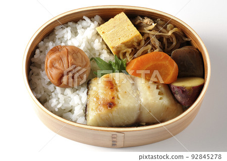 A bird's-eye view of a silver cod saikyo-yaki bento box with a large umeboshi on top of rice and tamagoyaki and simmered dishes on a white background 92845278
