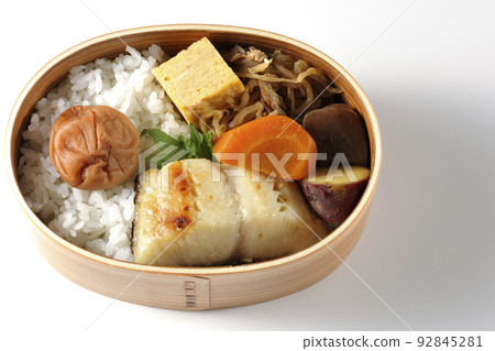 一個銀鱈魚西京燒便當盒的鳥瞰圖,在米飯和玉子燒上放著一個大醃李子,在白色背景上放著燉菜 一個銀鱈魚西京燒便當盒的鳥瞰圖,在米飯和玉子燒上放著一個大醃李子,在白色背景上放著燉菜 92845281