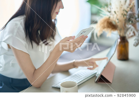 A woman operating a smartphone in front of a PC screen 92845900