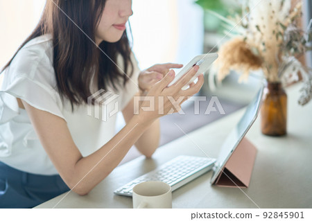 A woman operating a smartphone in front of a PC screen 92845901