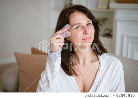Cute caucasian woman with jade gouache scraper in living room on sofa in 92845930
