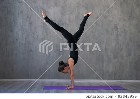 Attractive young woman doing yoga stretching yoga online at home against gray 92845959