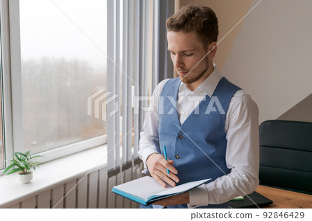 Thoughtful business man with beard in shirt and vest with notepad in his hand Thoughtful business man with beard in shirt and vest with notepad in his hand 92846429