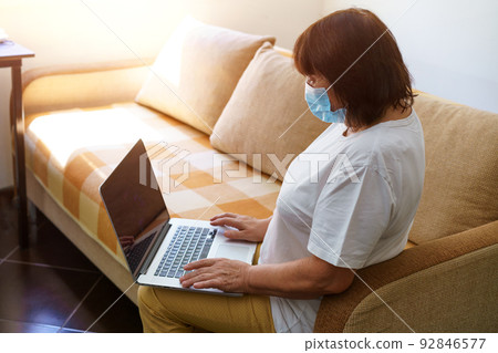 Serious woman in protective mask uses laptop, checks email on internet while 92846577