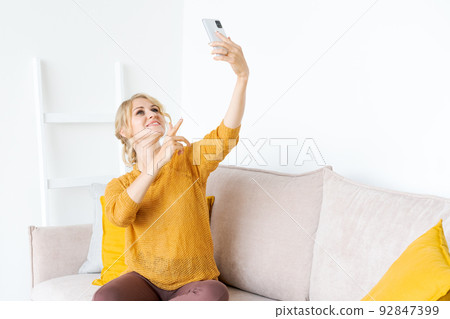 Smiling caucasian woman sitting on sofa at home, taking self portrait on modern 92847399