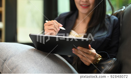 Smiling millennial woman using digital tablet while resting on couch at her personal office. Cropped shot Smiling millennial woman using digital tablet while resting on couch at her personal office. Cropped shot 92848072