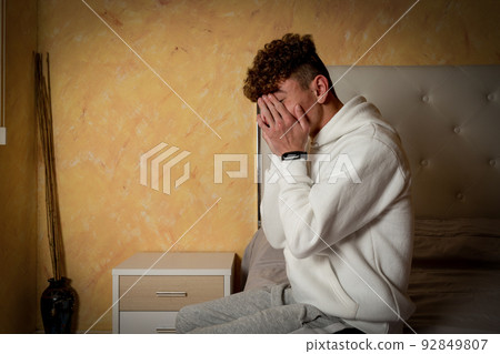 Stressed, depressed or grieving man sitting on bed covering face with hands and crying at home. Worried and frustrated male suffering depression or life crisis feeling desperate and hopeless 92849807