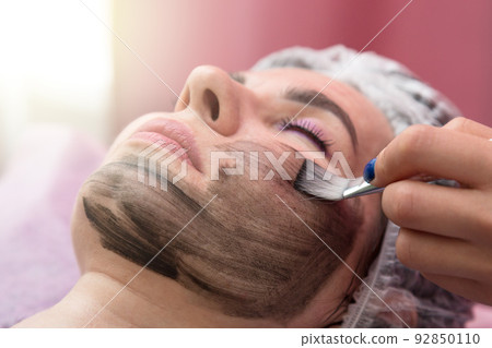 Portrait of an adult woman with her eyes closed during a carbon peeling procedure with a black mask on her face Portrait of an adult woman with her eyes closed during a carbon peeling procedure with a black mask on her face 92850110