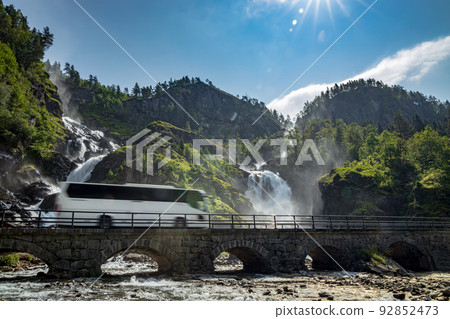 Tourist bus traveling on the road Latefossen Waterfall Odda Norway. Latefoss is a powerful, twin waterfall. Tourist bus traveling on the road Latefossen Waterfall Odda Norway. Latefoss is a powerful, twin waterfall. 92852473