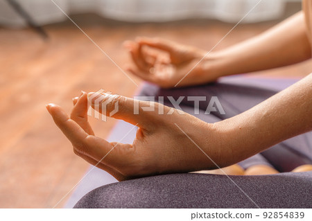 Young woman meditating in the lotus pose at home. Practicing yoga indoors. Harmony, yoga practice, balance, meditation, relaxation at home, healthy lifestyle concept. Young woman meditating in the lotus pose at home. Practicing yoga indoors. Harmony, yoga practice, balance, meditation, relaxation at home, healthy lifestyle concept. 92854839