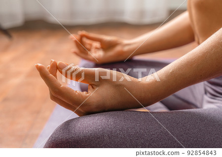 Young woman meditating in the lotus pose at home. Practicing yoga indoors. Harmony, yoga practice, balance, meditation, relaxation at home, healthy lifestyle concept. Young woman meditating in the lotus pose at home. Practicing yoga indoors. Harmony, yoga practice, balance, meditation, relaxation at home, healthy lifestyle concept. 92854843