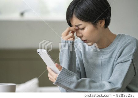 A young woman holding a smartphone and holding her head 92855253