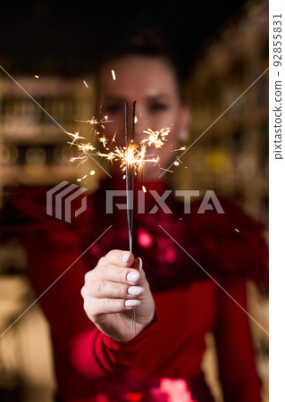 A girl in an elegant red dress holds sparklers in her hands A girl in an elegant red dress holds sparklers in her hands 92855831