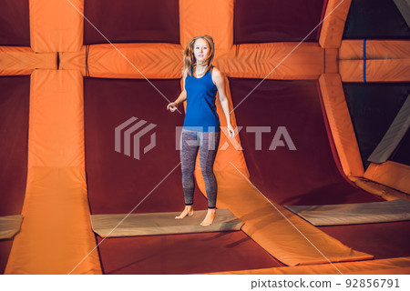Young woman sportsman jumping on a trampoline in fitness park and doing exersice indoors Young woman sportsman jumping on a trampoline in fitness park and doing exersice indoors 92856791