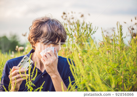 Young man sneezes because of an allergy to ragweed Young man sneezes because of an allergy to ragweed 92856866