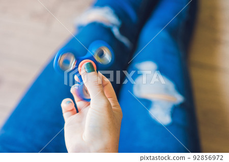 Girl teenager in holey jeans holds in hands and plays with spinner 92856972