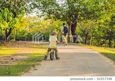 Happy family is riding bikes outdoors and smiling. Father on a bike and son on a balancebike 92857396