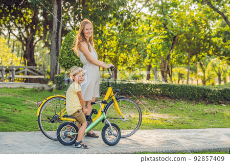 Happy family is riding bikes outdoors and smiling. Mom on a bike and son on a balancebike 92857409