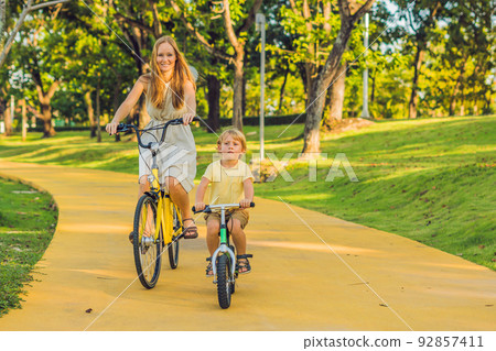 Happy family is riding bikes outdoors and smiling. Mom on a bike and son on a balancebike 92857411