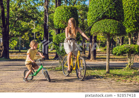 Happy family is riding bikes outdoors and smiling. Mom on a bike and son on a balancebike 92857418