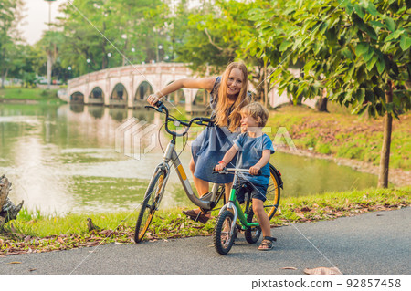 Happy family is riding bikes outdoors and smiling. Mom on a bike and son on a balancebike 92857458