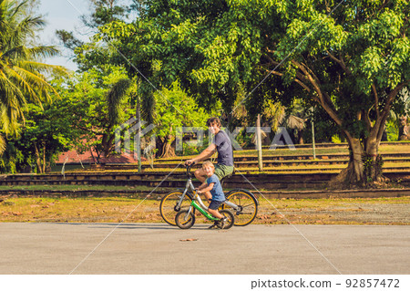Happy family is riding bikes outdoors and smiling. Father on a bike and son on a balancebike 92857472