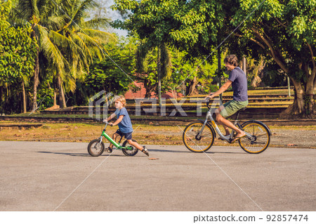 Happy family is riding bikes outdoors and smiling. Father on a bike and son on a balancebike 92857474