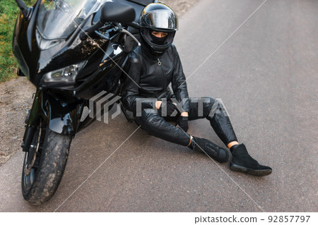 Biker girl in black outfit sits leaning on a motorcycle Biker girl in black outfit sits leaning on a motorcycle 92857797
