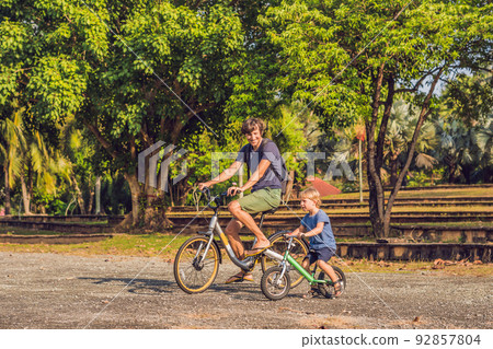 Happy family is riding bikes outdoors and smiling. Father on a bike and son on a balancebike 92857804