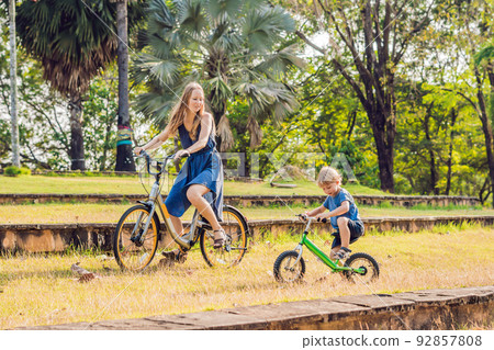 Happy family is riding bikes outdoors and smiling. Mom on a bike and son on a balancebike 92857808