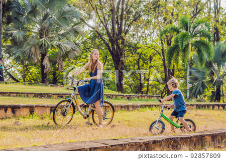 Happy family is riding bikes outdoors and smiling. Mom on a bike and son on a balancebike 92857809