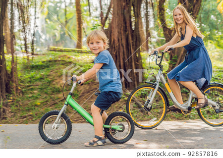 Happy family is riding bikes outdoors and smiling. Mom on a bike and son on a balancebike 92857816