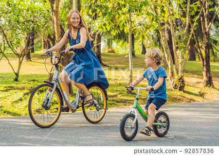 Happy family is riding bikes outdoors and smiling. Mom on a bike and son on a balancebike 92857836