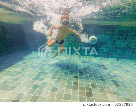 A child boy is swimming underwater in a pool, smiling and holding breath, with swimming glasses A child boy is swimming underwater in a pool, smiling and holding breath, with swimming glasses 92857926