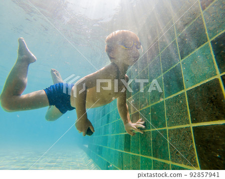 A child boy is swimming underwater in a pool, smiling and holding breath, with swimming glasses A child boy is swimming underwater in a pool, smiling and holding breath, with swimming glasses 92857941