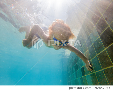 A child boy is swimming underwater in a pool, smiling and holding breath, with swimming glasses A child boy is swimming underwater in a pool, smiling and holding breath, with swimming glasses 92857943