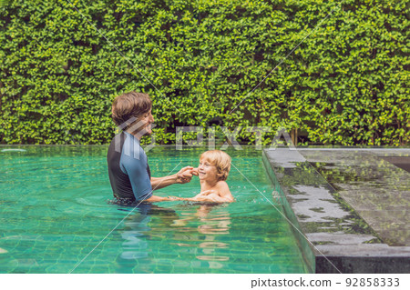 Male instructor swimming for children teaches a happy boy to swim in the pool Male instructor swimming for children teaches a happy boy to swim in the pool 92858333
