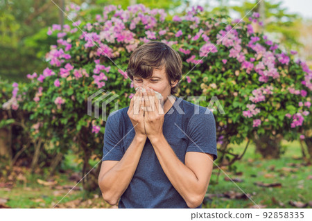 Young man sneezes because of an allergy to pollen Young man sneezes because of an allergy to pollen 92858335