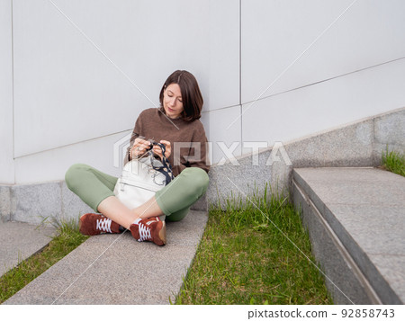 Woman is crocheting outdoor. Tranquil leisure of female in urban park. Anti-stress hobby. 92858743