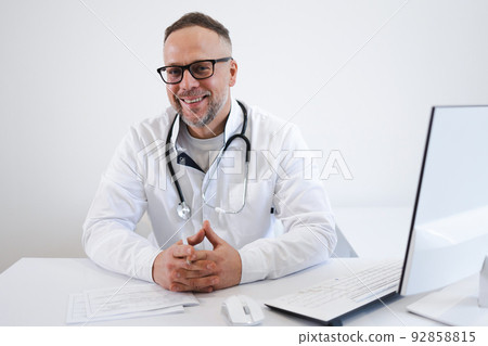 Portrait of a happy male doctor sitting at his desk in the office 92858815